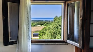Una stanza con una finestra che si affaccia su un paesaggio con alberi e una vista lontana del mare.
