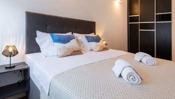 A hotel room with a bed, pillows, a nightstand, a lamp, and a wardrobe.