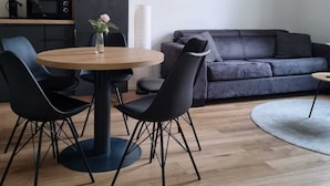 A modern living room with a round wooden table, black chairs, a dark grey sofa, and a small coffee table.