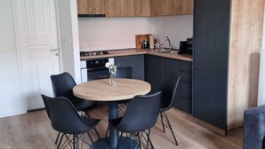 A modern kitchen with wooden cabinets, a round dining table with chairs, and a grey sofa.