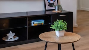 A living room with a round wooden table, a black entertainment unit, a framed artwork, and a small potted plant.