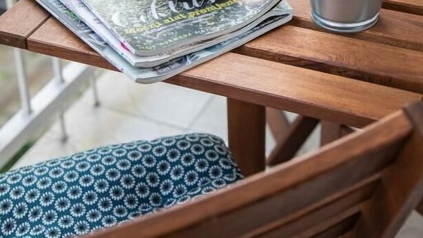 A wooden table with a white cup and saucer, a small potted plant, and a stack of magazines.