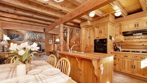 A wooden cabin interior with a dining area, kitchen, and a fireplace. - Binky's Mountain Hideaway #2455 (Big Bear Lake)