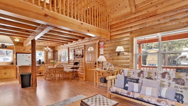 A cozy log cabin interior with a dining area, a sofa with patterned cushions, and a chessboard on a table. - Binky's Mountain Hideaway #2455 (Big Bear Lake)