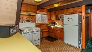A compact kitchen with wooden cabinets, a built-in stove, a refrigerator, and a window providing natural light. - Makin' Memories AT Summit #1683 (Big Bear Lake)