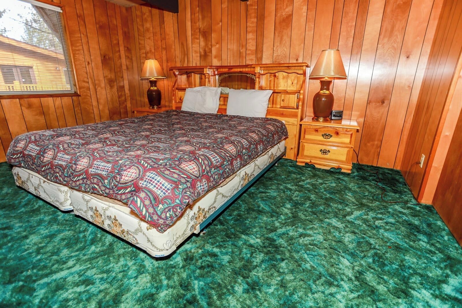 A wooden-paneled room with a bed, two nightstands, and a window.