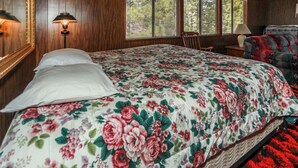 A bedroom with a floral bedspread, a wooden headboard, a nightstand with a lamp, and a window with blinds. - Makin' Memories AT Summit #1683 (Big Bear Lake)