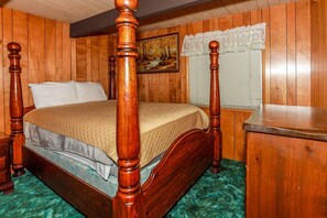 Un lit à baldaquin avec une structure en bois et une tête de lit rembourrée de tissu vert, placé devant un mur lambré en bois.