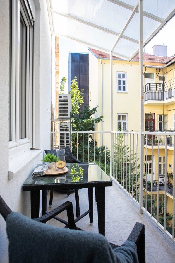 A balcony with a table and chairs, overlooking a courtyard with buildings.