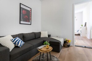 A modern living room with a sectional sofa, a small round table with a plant, and a framed artwork on the wall.