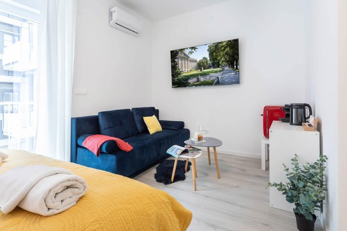 Habitación de hotel moderna con cama, sofá, una mesita, cafetera y planta.