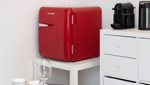 Um quarto pequeno com um eletrodoméstico vermelho, uma cafeteira e uma revista sobre uma mesinha.