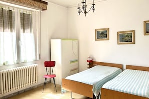 Une chambre à coucher comprenant un lit, une chaise, un radiateur, une fenêtre avec des rideaux et des tableaux accrochés au mur.