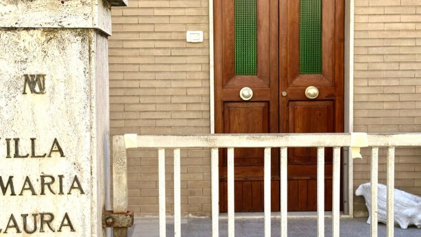 Entrada de un edificio con una reja metálica, una puerta de madera con detalles verdes y un cartel con texto parcialmente visible.