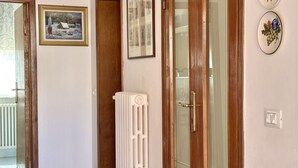 Un pasillo con un radiador, una puerta con panel de vidrio y dos cuadros en la pared.