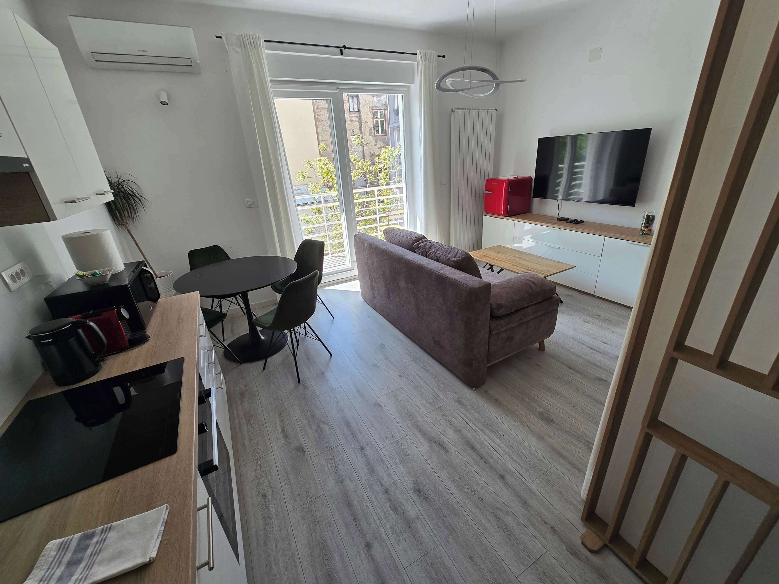 A modern living space with a dining area, sofa, kitchen, and a TV.