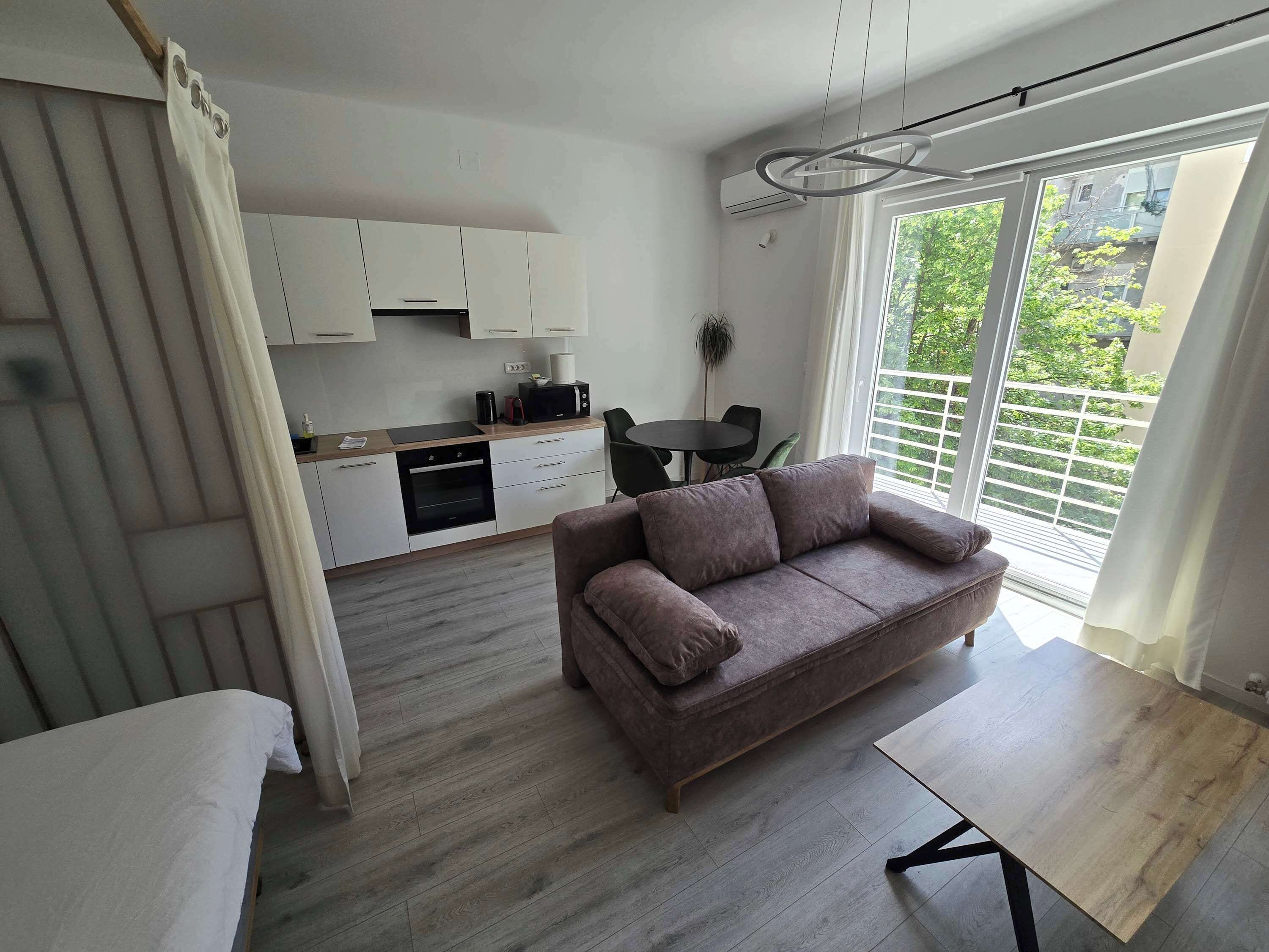 A modern living space with a sofa, a dining table, a kitchen area, and a large window with a view.