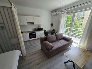 Moderni olohuone, jossa on sohva, ruokapöytä, keittiö ja suuri ikkuna, josta on kaunis näköala.