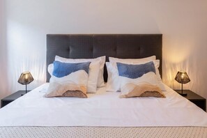 Ein ordentlich bezogenes Bett mit weißer Bettwäsche und zwei Zierkissen, beidseits flankiert von Nachttischlampen.