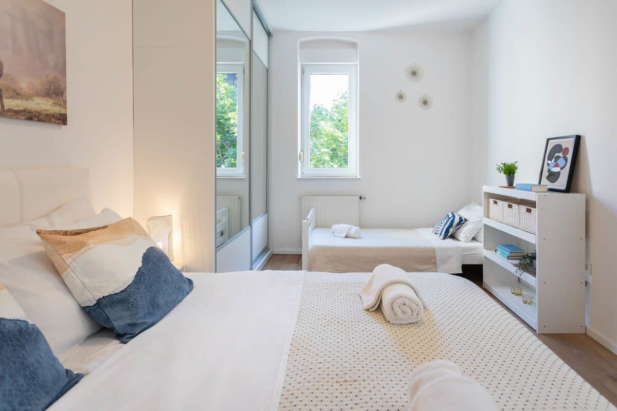 Een hotelkamer met een groot bed, een kleiner bed, een raam, een verwarming en een boekenplank.