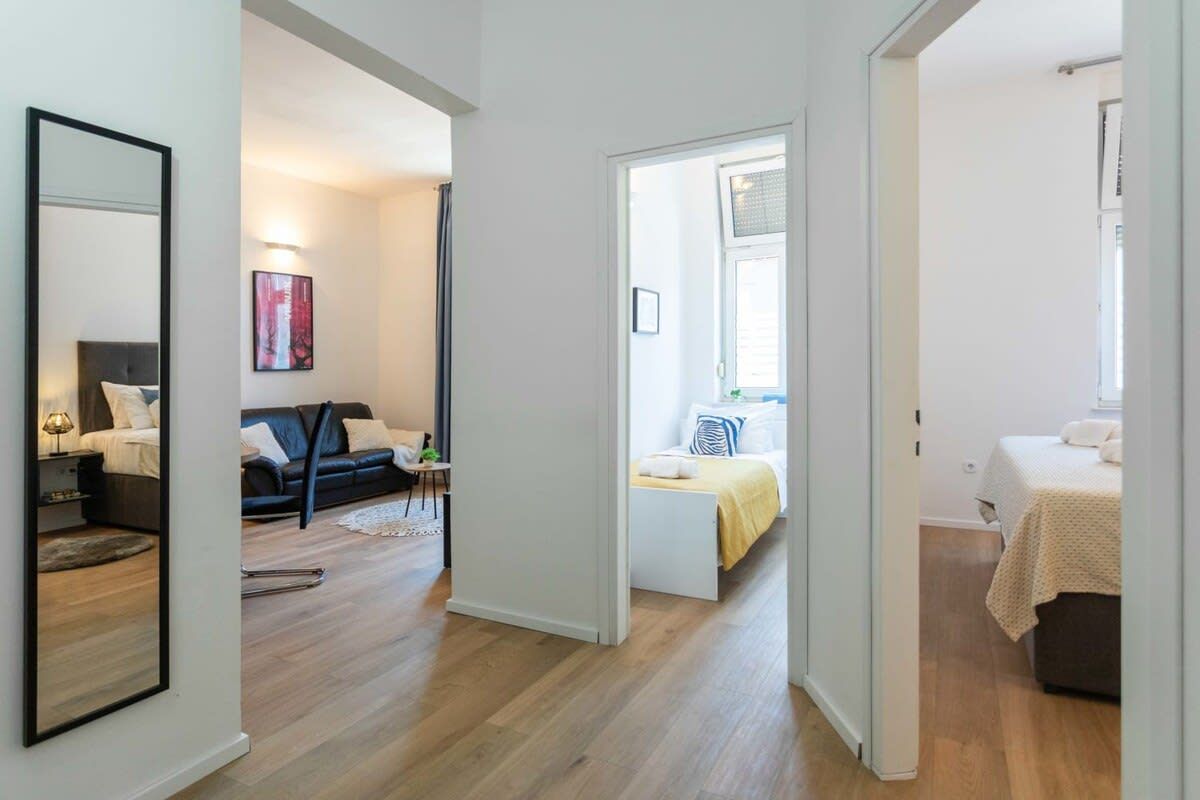 A modern apartment with a living area, a bedroom, and a bathroom. There is a sofa set, a bed, and a mirror.