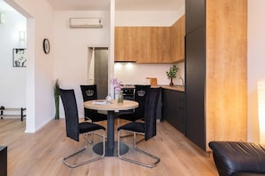 A modern kitchen with wooden cabinets, a dining area with a round table and black chairs, and a black leather sofa.