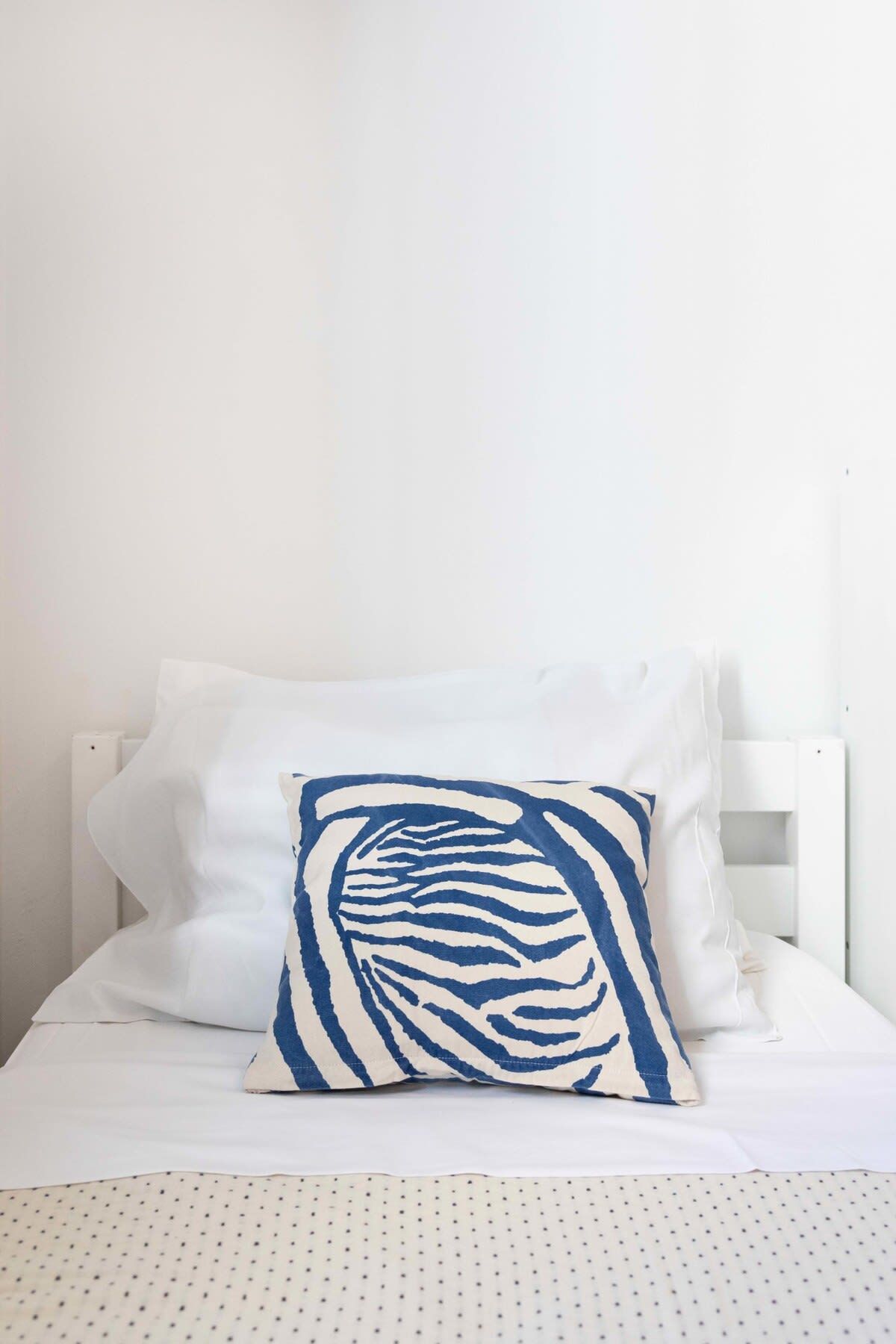 A bed with white bedding and a single blue and white patterned pillow.