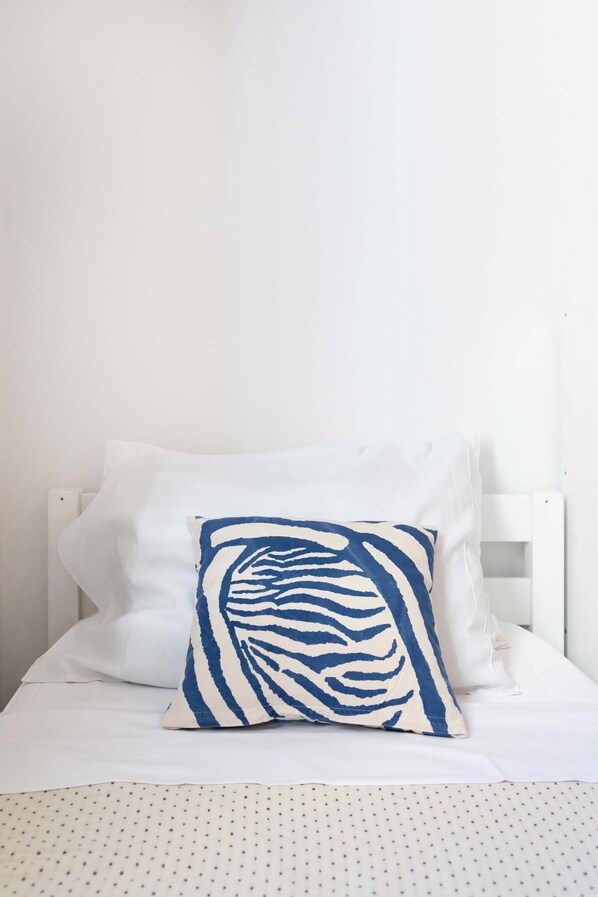 A bed with white bedding and a single blue and white patterned pillow.