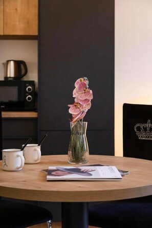 Ein runder Holztisch mit einer klaren Glasvase, in der rosa Orchideen, eine Zeitschrift und zwei weiße Tassen mit schwarzen Griffen stehen.
