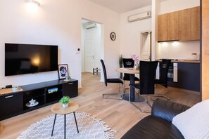 A modern living room with a flat-screen TV, a dining area with a table and chairs, and a kitchen with wooden cabinets.