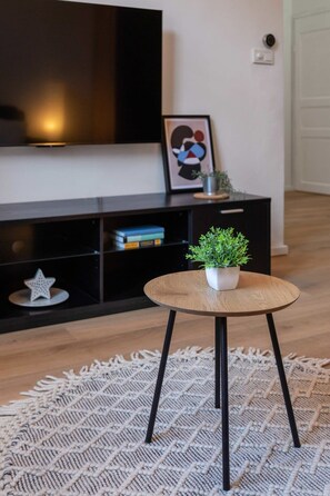 A modern living room with a round wooden table, a black entertainment unit, and a woven rug.