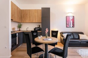 A modern kitchen with wooden cabinets, a black refrigerator, and a dining area with a round table and black chairs.