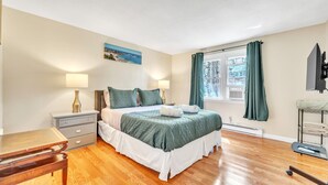 Een slaapkamer met een bed, nachtkastjes, een bureau, een raam met gordijnen, een schilderij aan de muur en een aan de muur bevestigde televisie.
