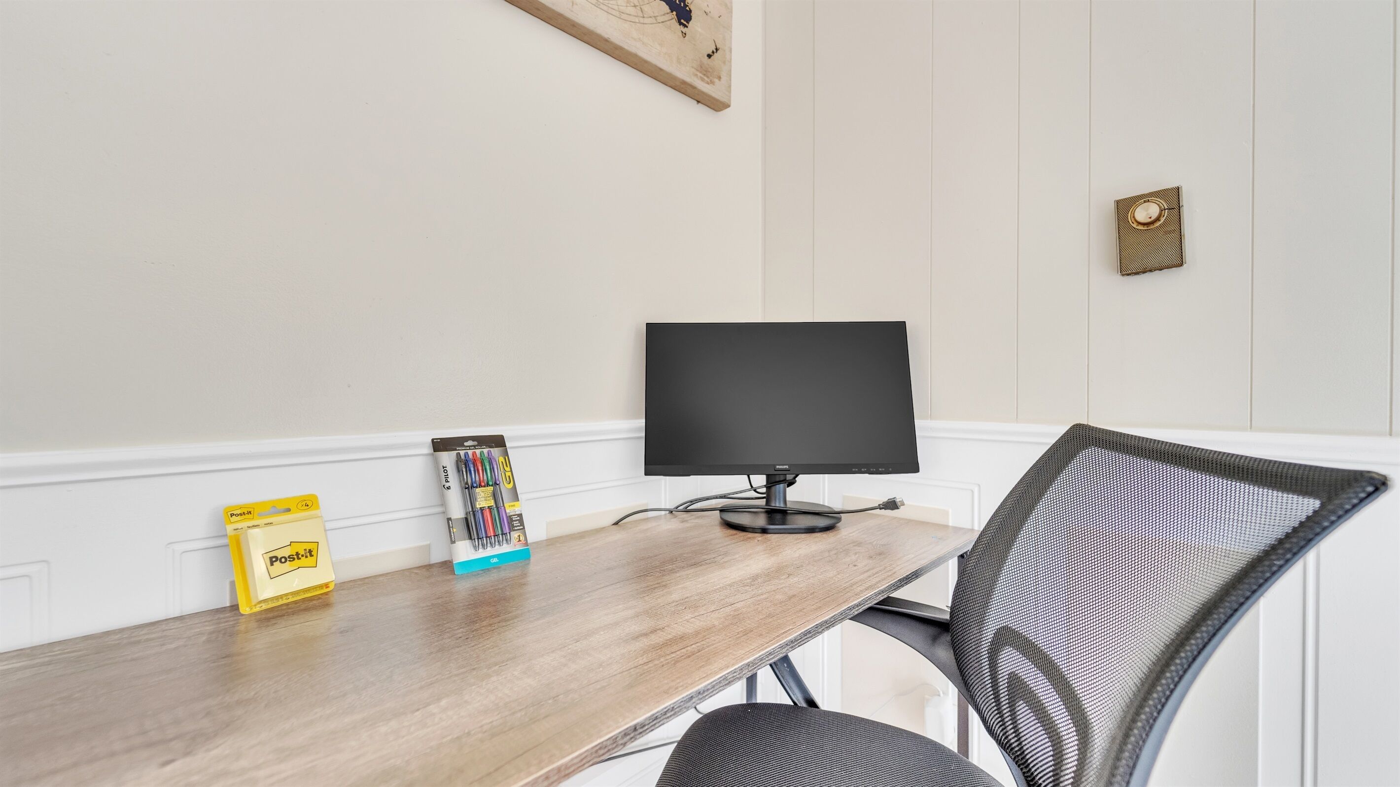 A wooden desk with a computer monitor, a chair, and stationery items.