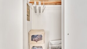 Een slaapkamer met een bed, een klein opbergmeubel en een kapstok met keukengerei.