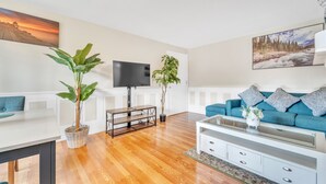 Een moderne woonkamer met een houten vloer, een blauwe bank, een witte salontafel en twee planten in potten.