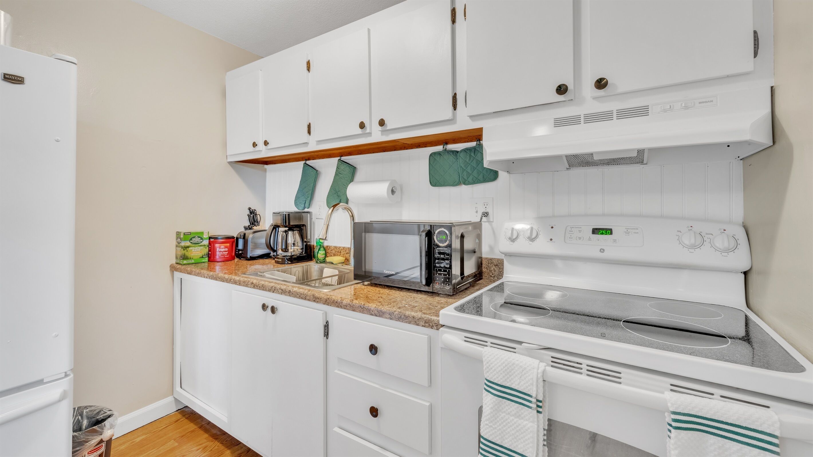 Una cocina compacta con armarios blancos, un microondas, un tostador y una estufa.