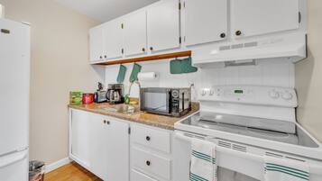 Una cocina compacta con armarios blancos, un microondas, un tostador y una estufa.
