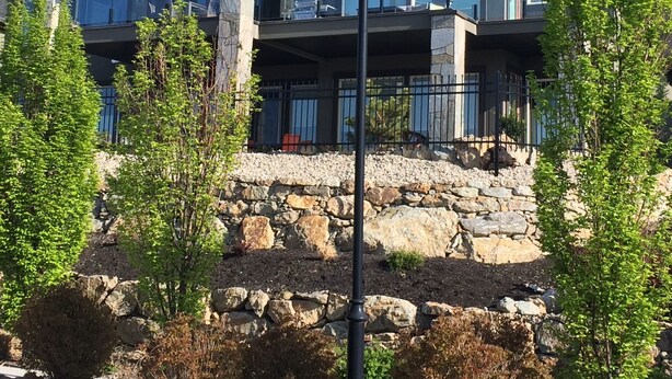 Una casa moderna de dos pisos con base de piedra, ventanas amplias y un balcón.