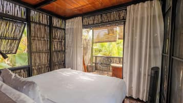 Um quarto com uma cama, uma cadeira, uma mesinha e um ventilador.