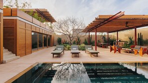 Un espace piscine extérieur moderne, doté de chaises longues, d’une pergola et d’un grand arbre au centre.