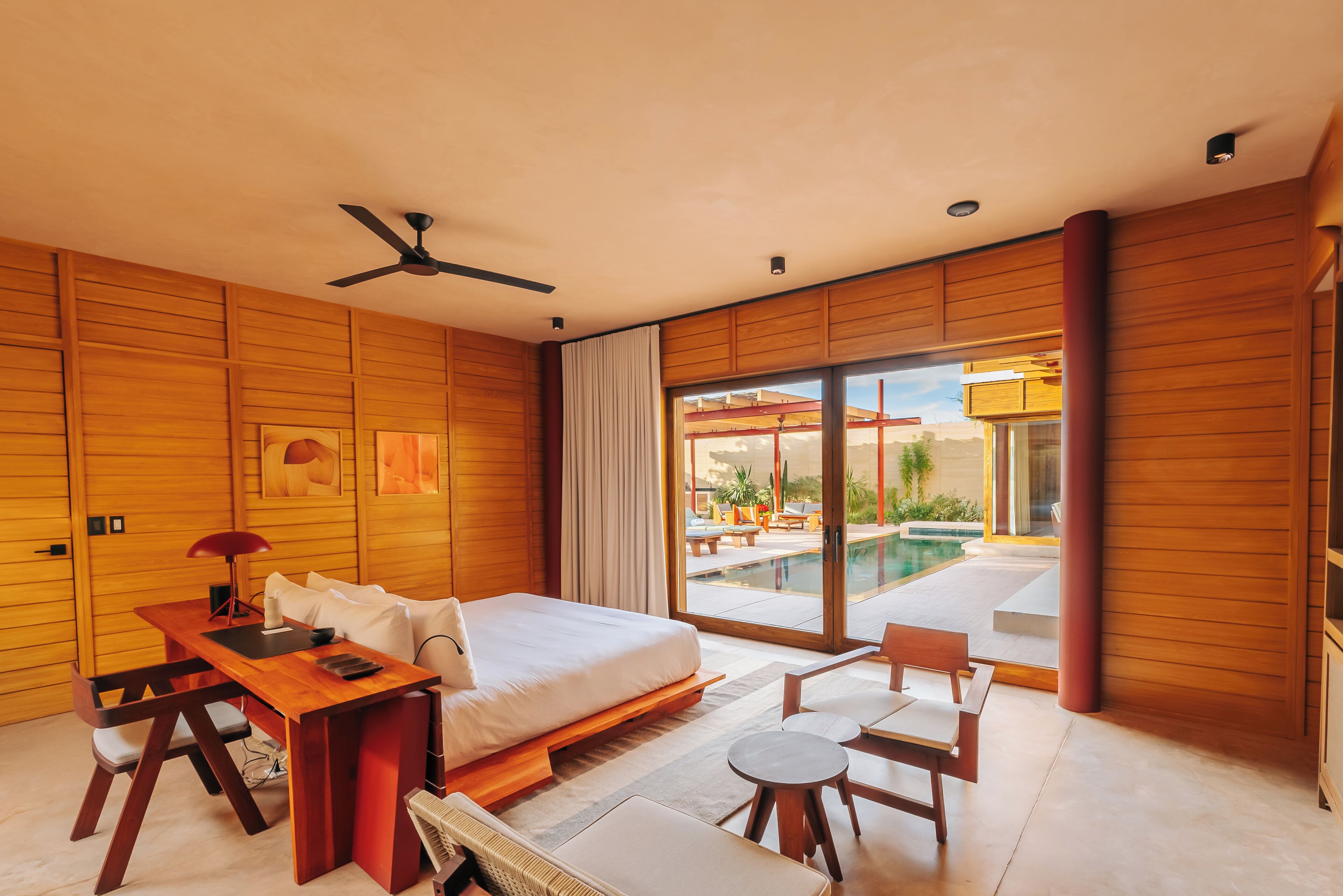 A modern bedroom with a bed, a desk, and a view of a swimming pool.