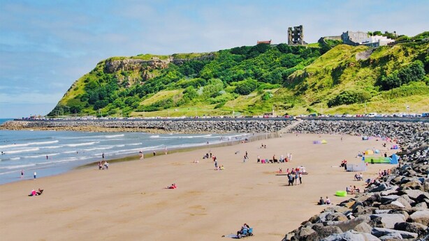 A beach with a rocky shoreline, a castle on a hill, and people enjoying the beach.