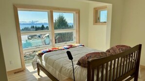 Ein Schlafzimmer mit großem Fenster, einem Bett, einem Nachttisch und Blick auf eine Berglandschaft.