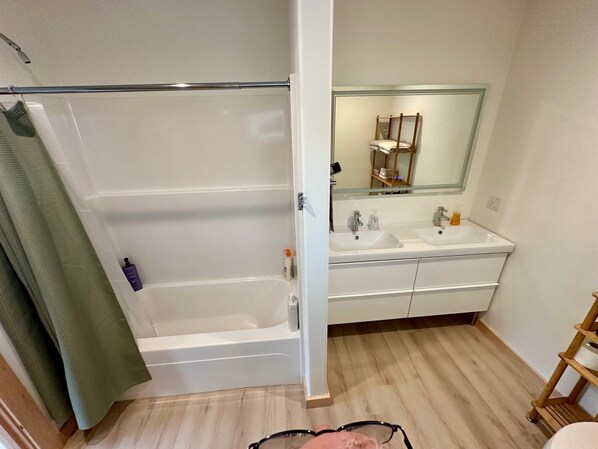 A bathroom with a bathtub, two sinks, a mirror, and a wooden shelf.