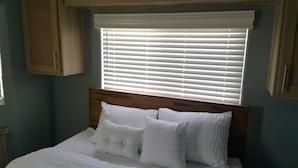 Ein Schlafzimmer mit einem Holzkopfende, weißer Bettwäsche und einem Fenster mit Jalousien.