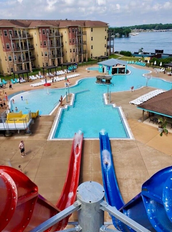 A hotel pool area with two water slides, a lifeguard tower, and a view of a body of water.