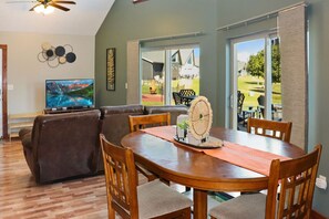 A dining area with a wooden table and chairs, a television, and a view of the outdoors.