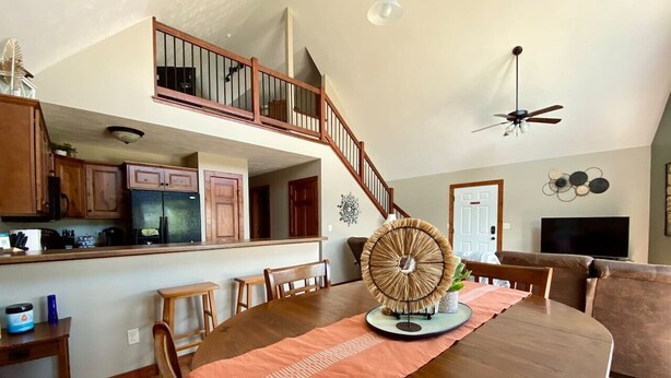 Un comedor espacioso con una gran mesa de madera, un abanico decorativo y una escalera que conduce a un nivel superior.