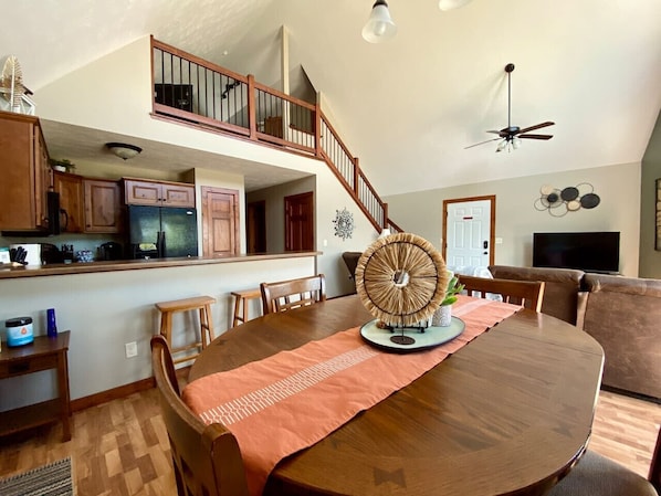 A spacious dining area with a large wooden table, a decorative fan, and a staircase leading to an upper level.